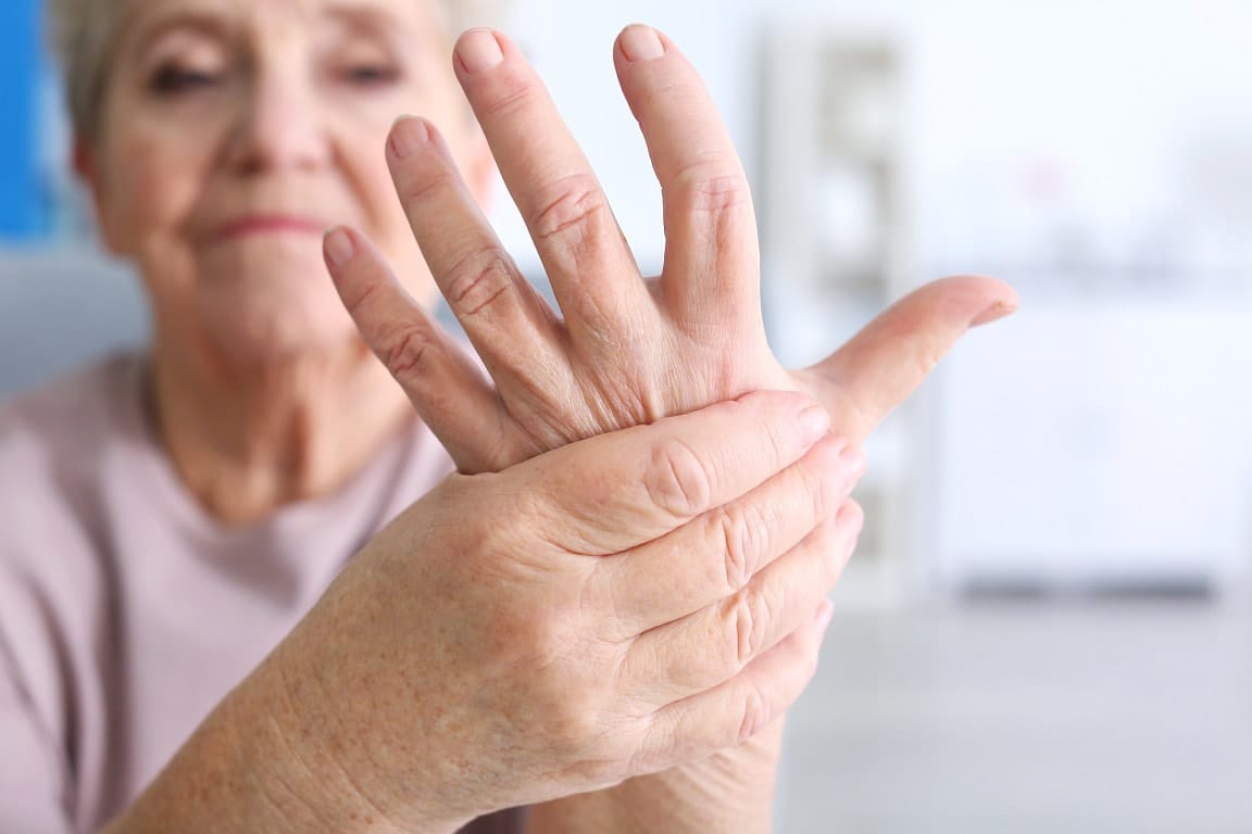 Senior with arthritis squeezes hand for pain relief.