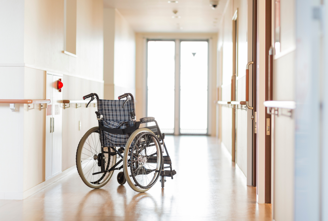 An unoccupied wheelchair parked along a bright, clean corridor in an assisted living facility
